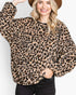 A woman wearing a fuzzy leopard-print long-sleeve top with black trim, paired with black jeans and a brown hat, against a plain white background.