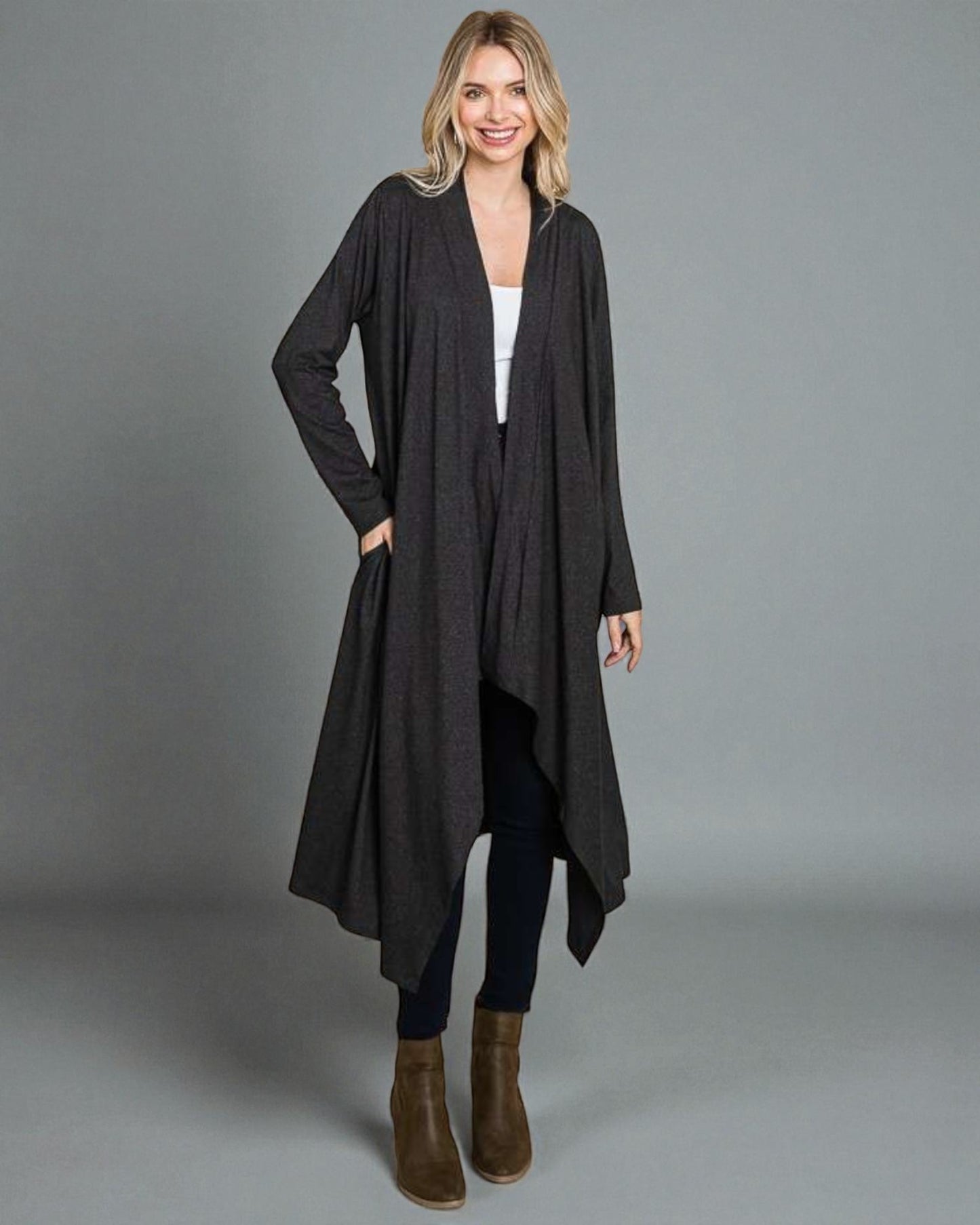 Woman wearing a long black cardigan over a white top and dark pants on a gray background
