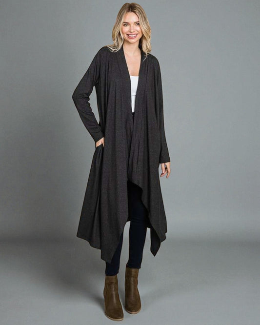 Woman wearing a long black cardigan over a white top and dark pants on a gray background