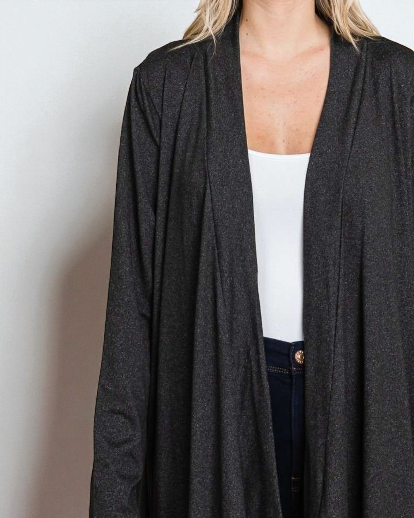 Person wearing a dark gray cardigan over a white top and dark pants on a plain background