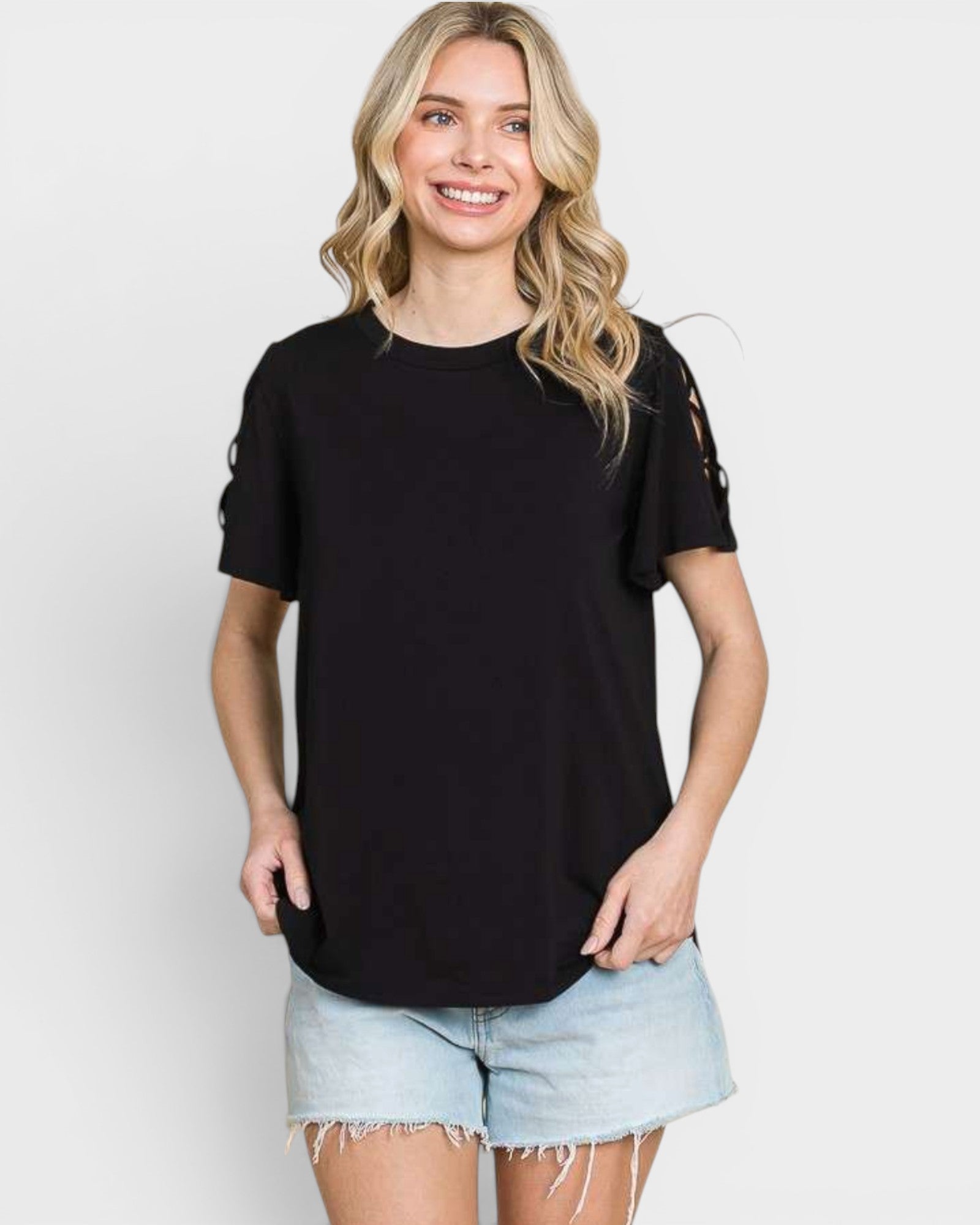 A woman wearing a black short-sleeve t-shirt with distressed details on the sleeves and light wash denim shorts, standing against a light gray studio background.