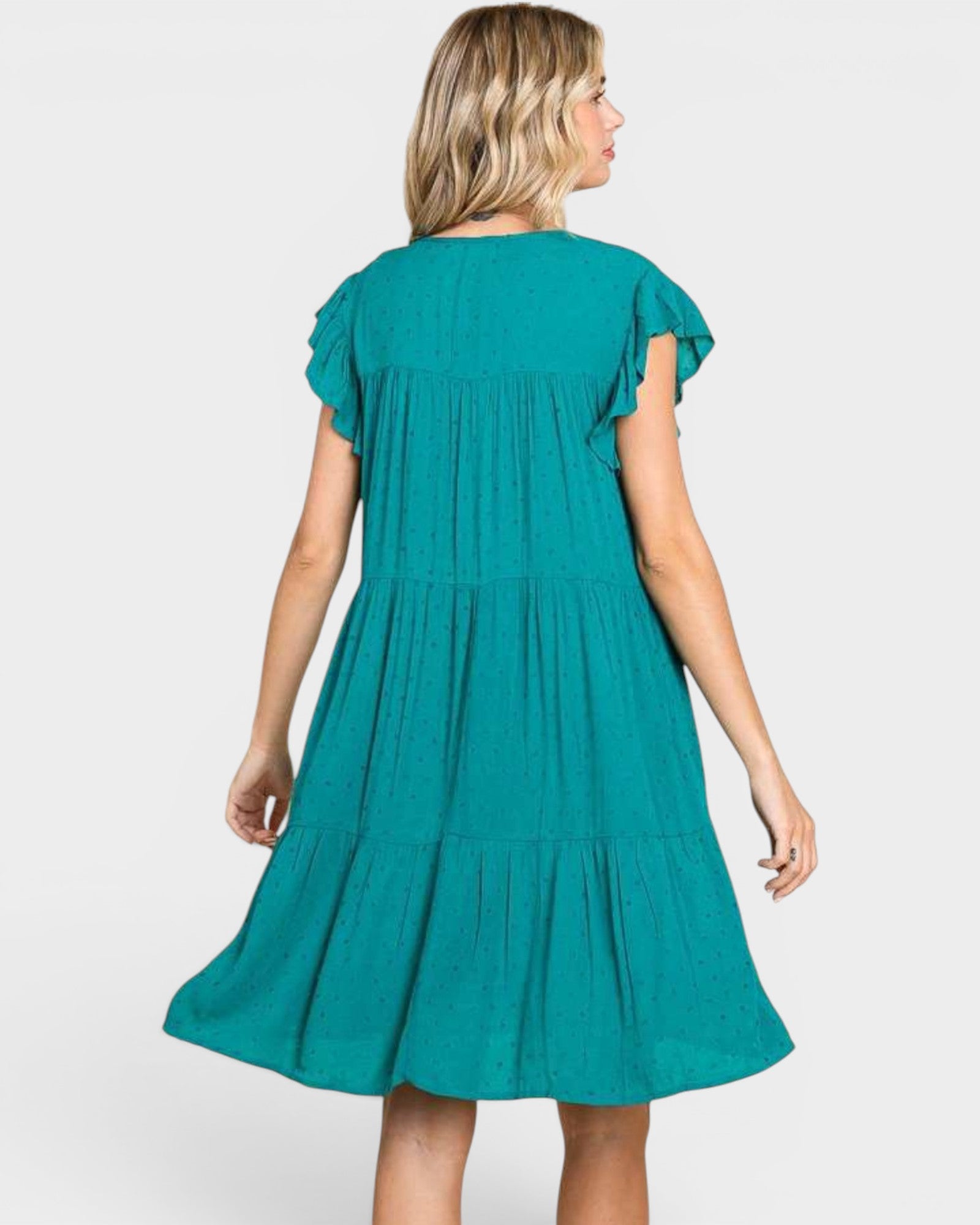 A woman wearing a teal green tiered dress, shown from the back against a light gray studio background.