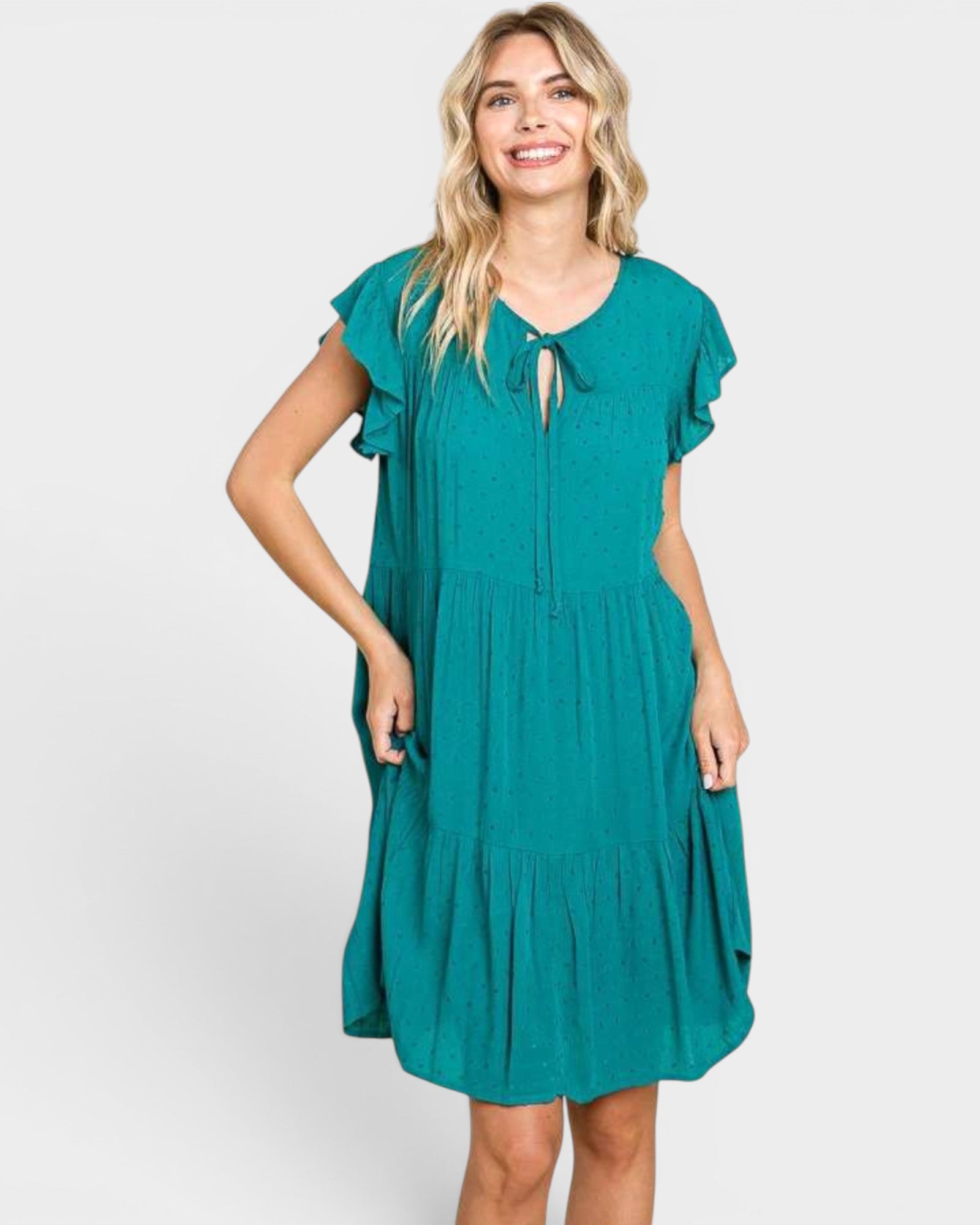 A woman modeling a teal green tiered midi dress with short flutter sleeves, a split neckline with a keyhole tie, and side pockets, set against a plain light gray background.