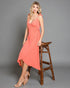 Woman in a coral dress standing next to a wooden stool on a gray background