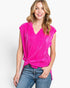 A woman wearing a bright hot pink corduroy wrap-style top with a twisted knot detail at the waist, paired with blue jeans, against a plain white studio background.