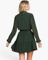 A woman shown from the back wearing a dark green long-sleeve mini dress with a subtle polka dot pattern, set against a plain white studio background.