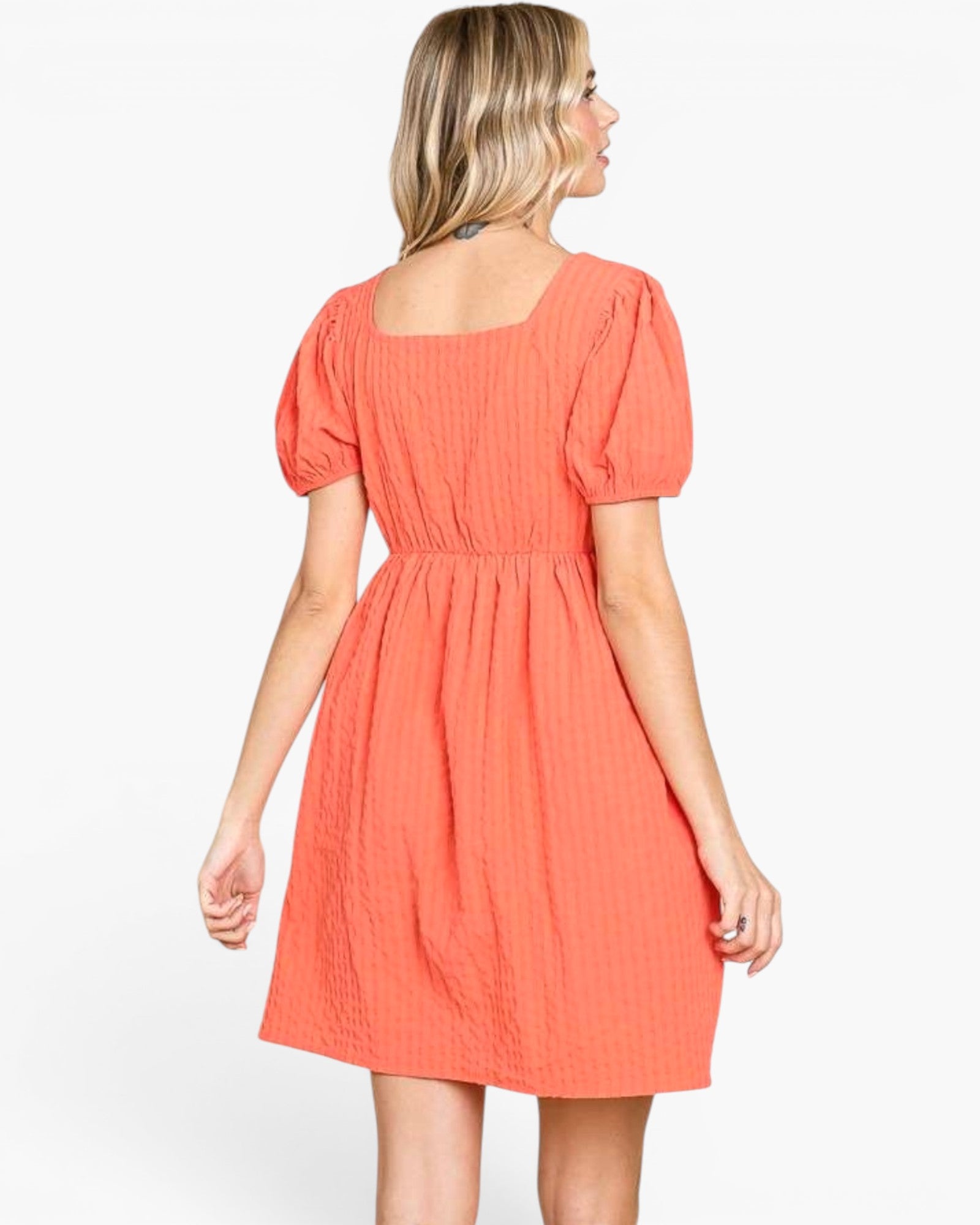 A woman shown from the back wearing a short puff-sleeve dress in a textured coral-orange color, set against a plain white studio background.