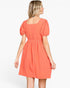 A woman shown from the back wearing a short puff-sleeve dress in a textured coral-orange color, set against a plain white studio background.