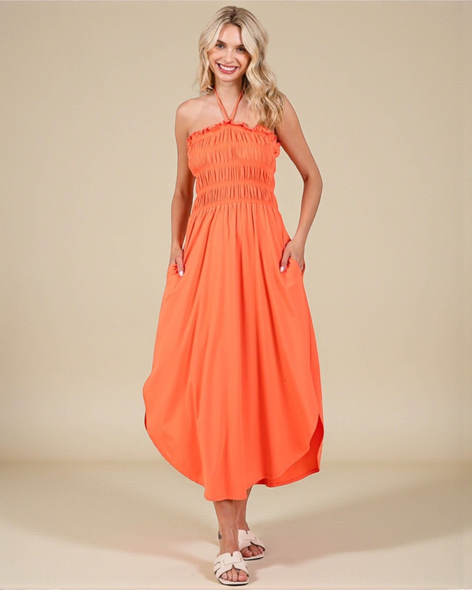 Woman wearing an orange halter neck dress on a beige background