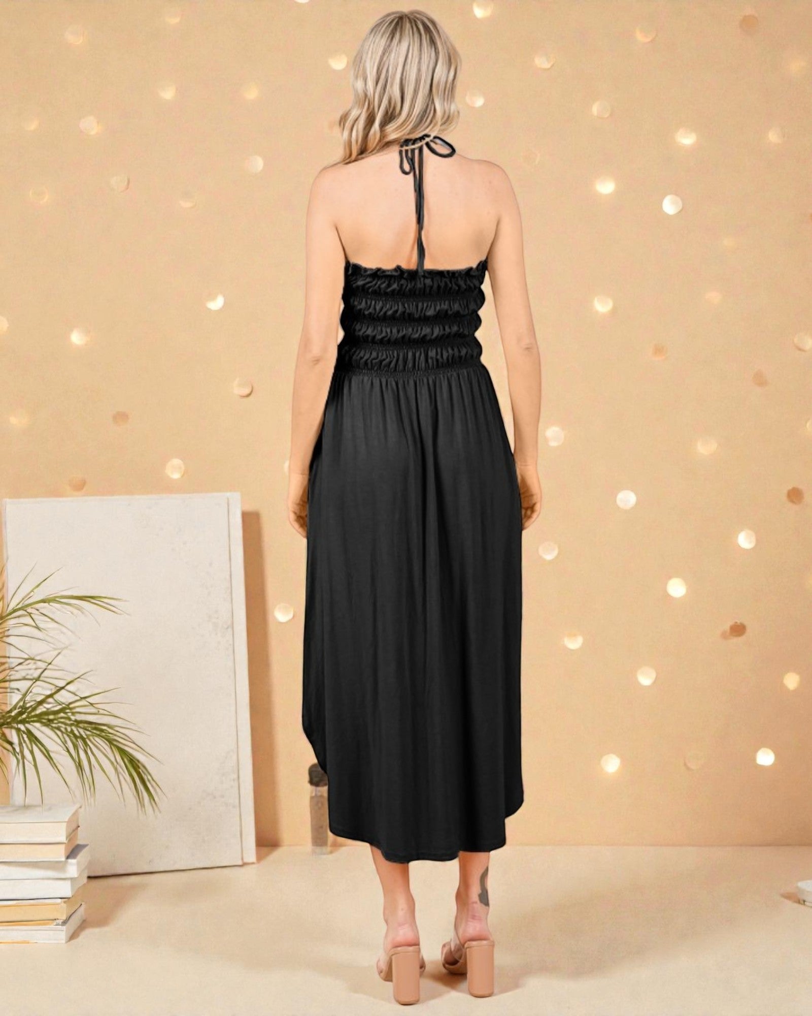 Woman wearing a black dress against a warm-toned wall with string lights