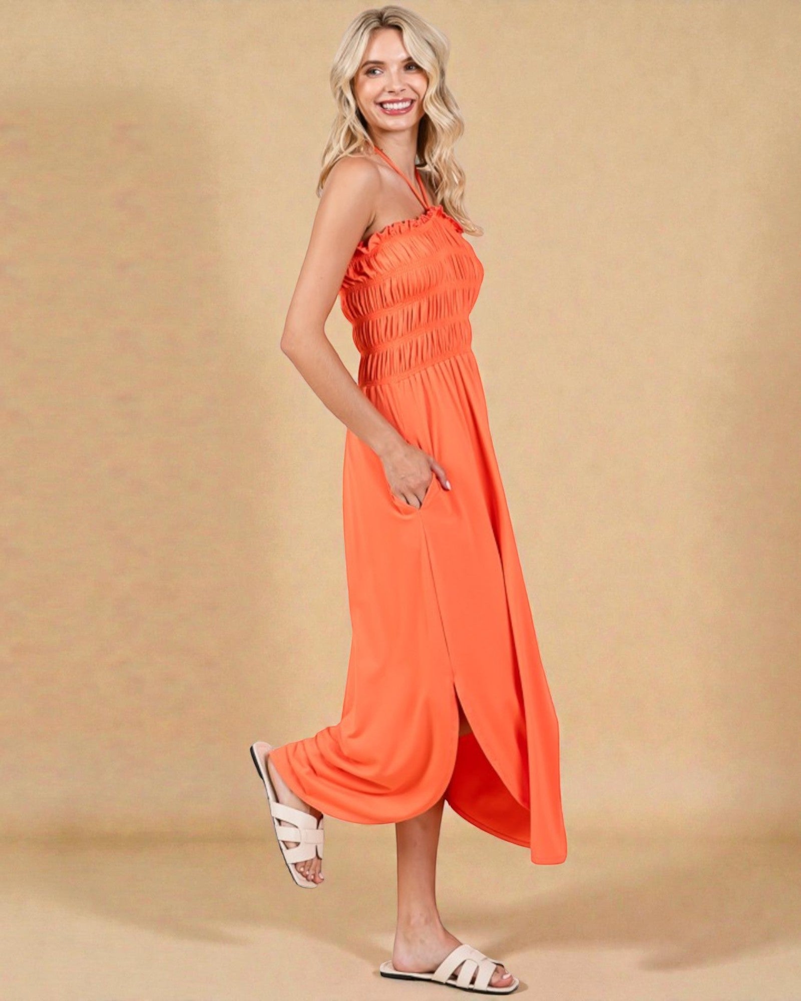 Woman wearing an orange halter neck dress on a beige background