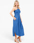 A woman modeling a blue halter-neck midi dress with a gathered waist and side pockets, paired with beige heeled sandals, against a plain white studio background.