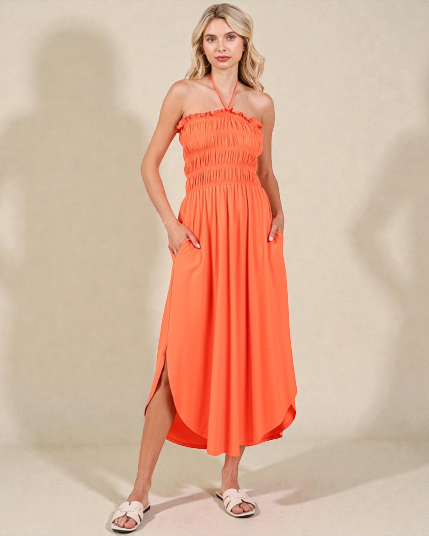 Woman wearing an orange halter neck dress with a slit on a beige background