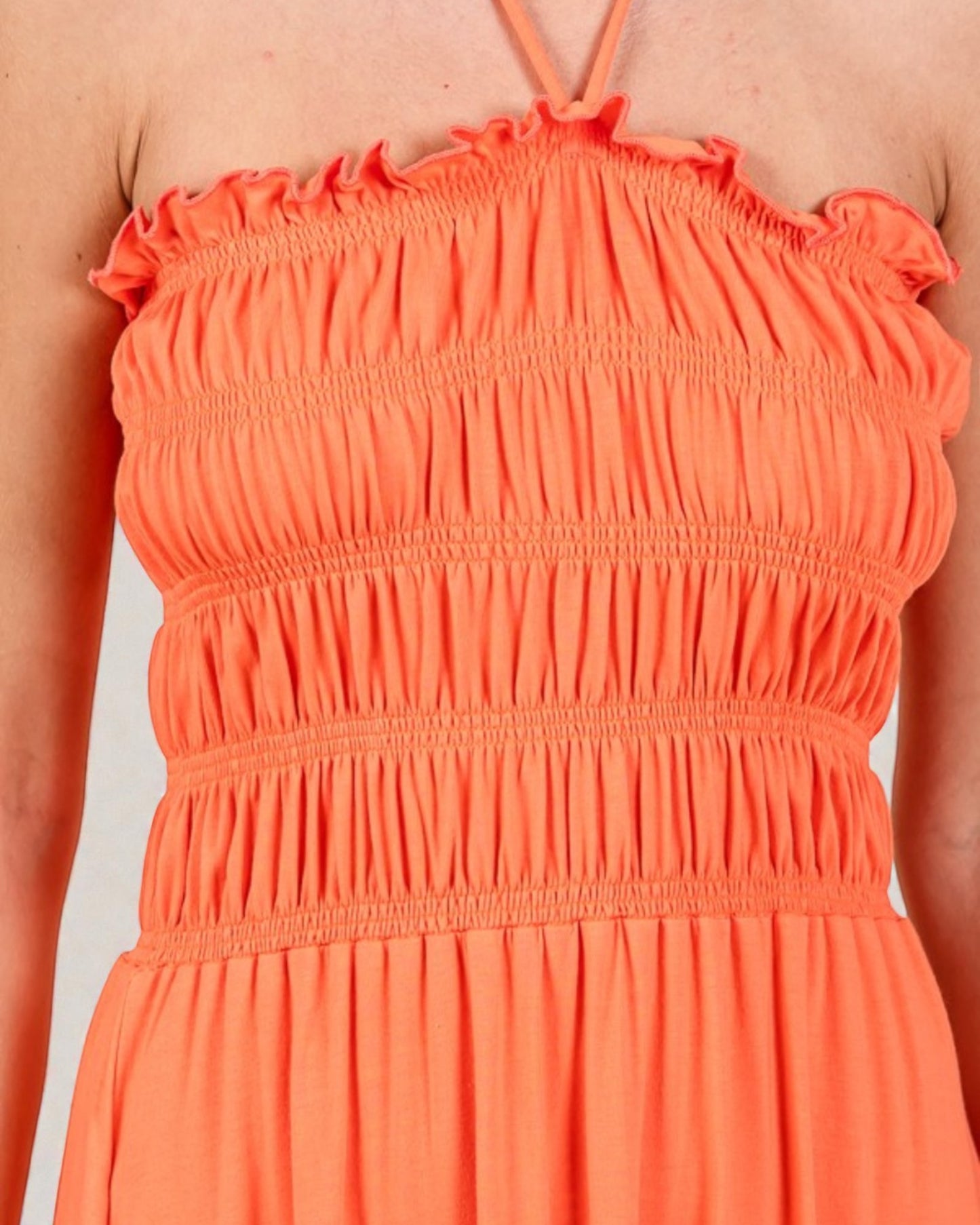 Close-up of an orange dress with ruffled straps on a neutral background