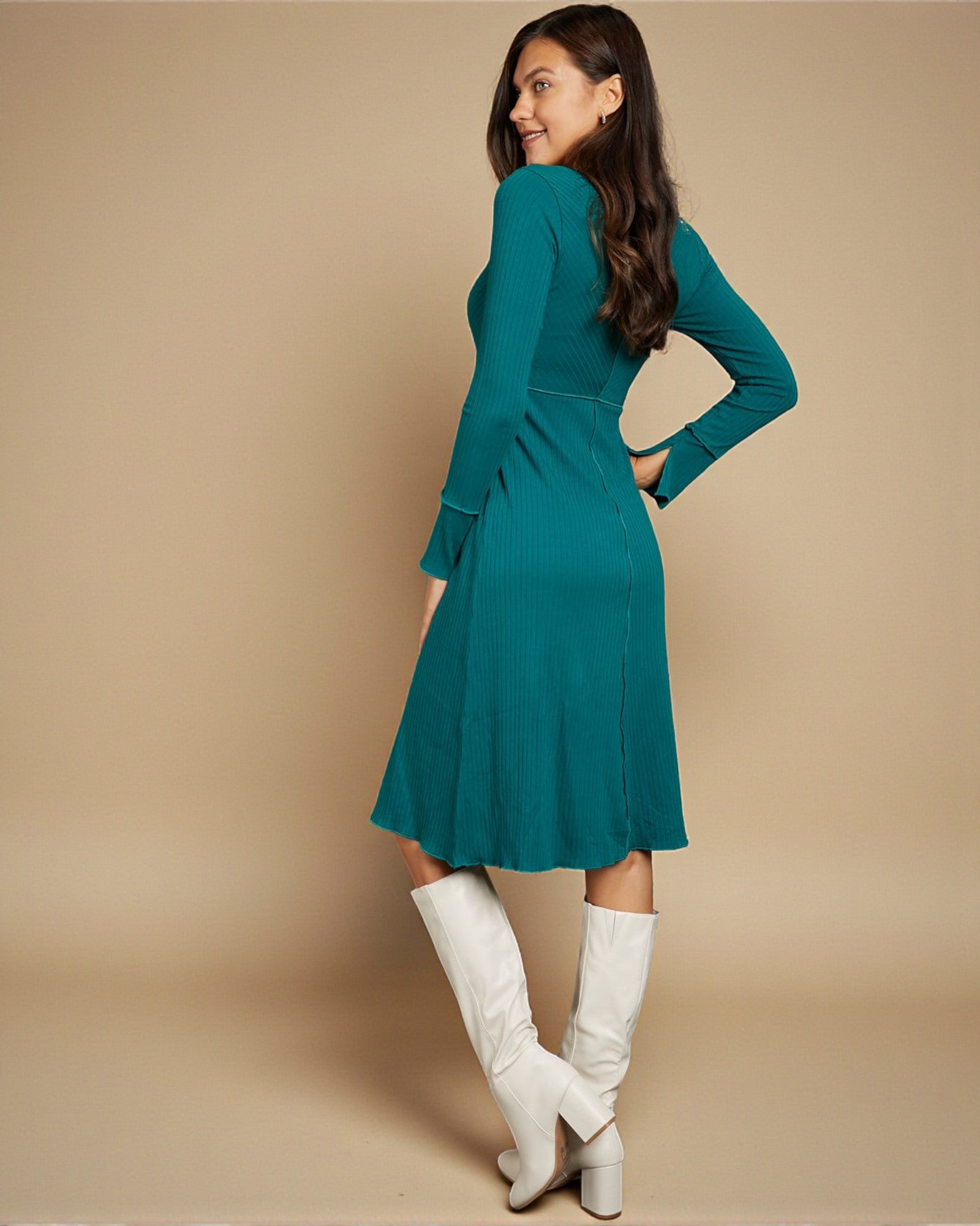Woman wearing a teal dress with long sleeves and white knee-high boots on a beige background