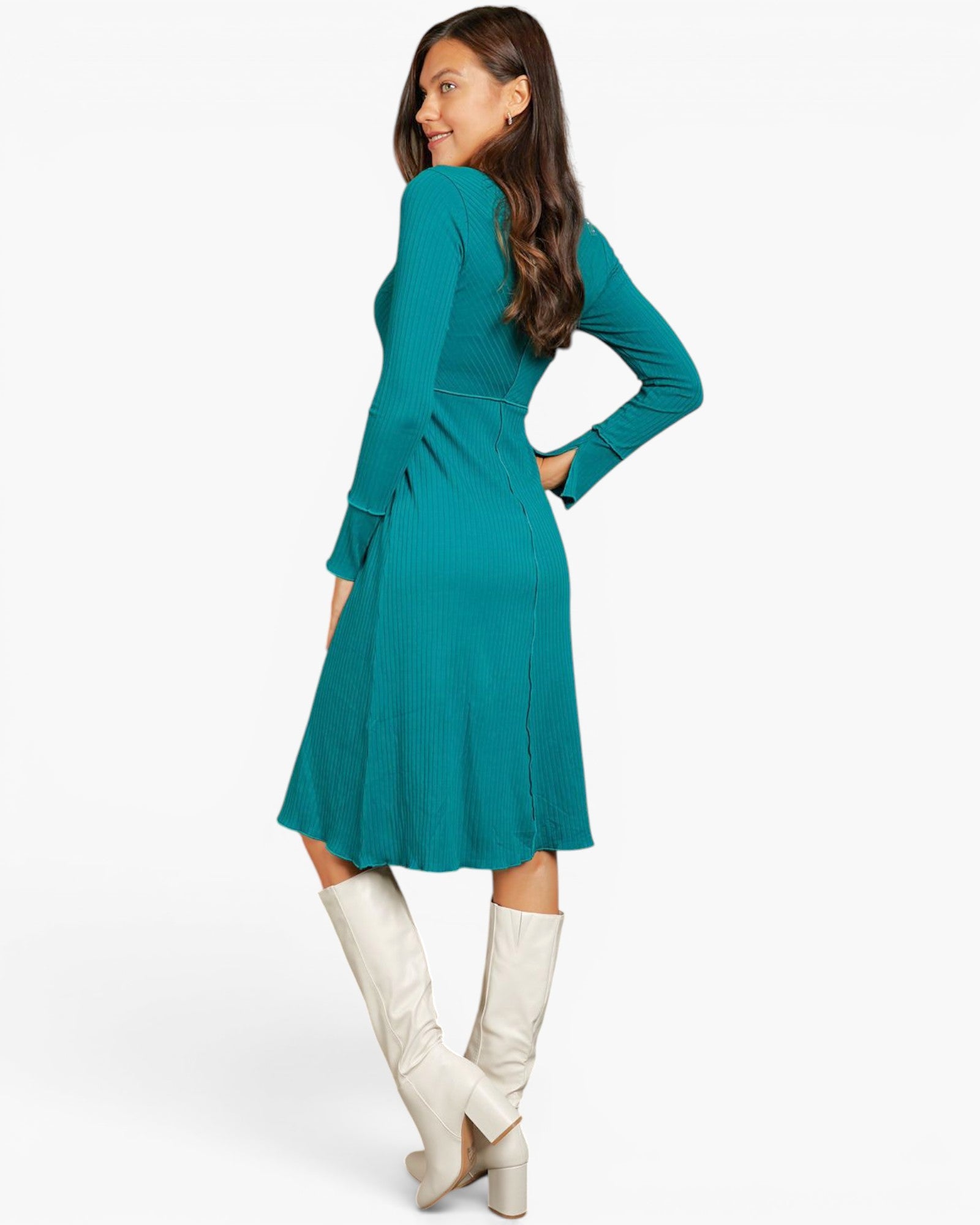 A woman modeling a teal long-sleeve midi dress with a flared skirt, paired with off-white knee-high boots, shown from a three-quarters back angle against a plain white studio background.