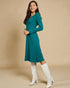 Woman wearing a teal dress and white knee-high boots against a beige background