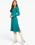 A woman modeling a teal long-sleeve V-neck midi dress with a flared skirt, paired with off-white knee-high boots, against a plain white studio background.