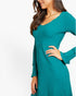 A woman wearing a teal green long-sleeve ribbed dress, shown from the side against a plain white background.