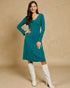 Woman wearing a teal dress and white knee-high boots against a beige background