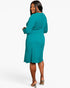 A woman modeling a teal long-sleeve ribbed knit midi dress, shown from a back-three-quarter angle against a plain white studio background.