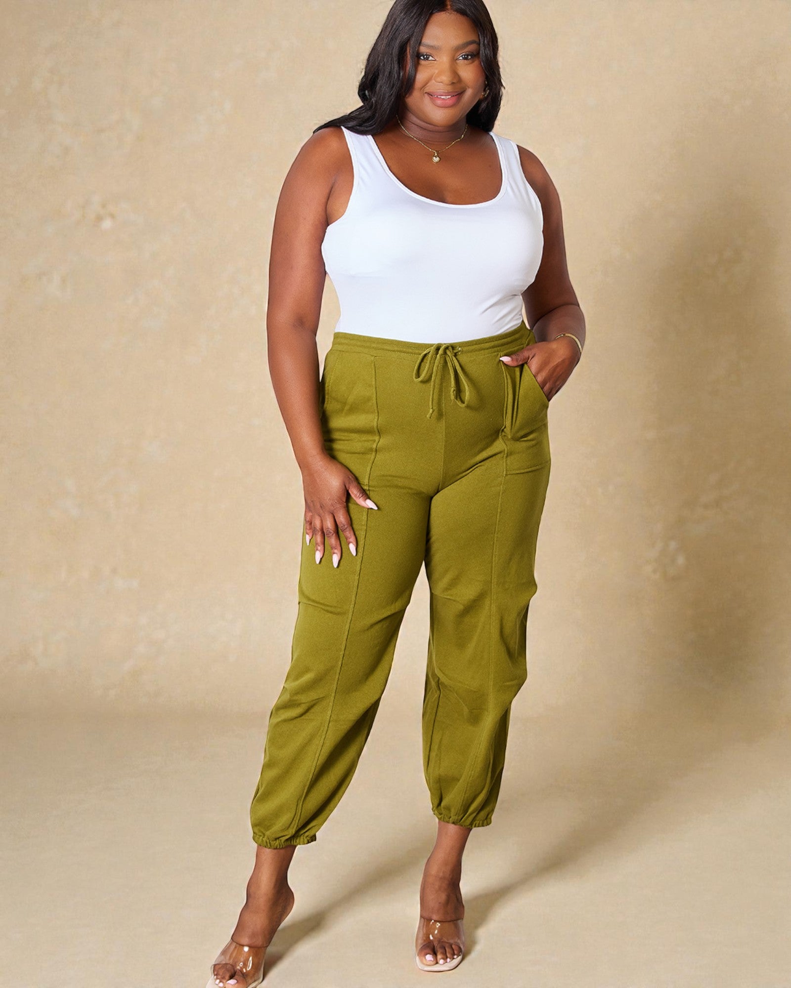 Woman wearing green pants and a white top against a beige background