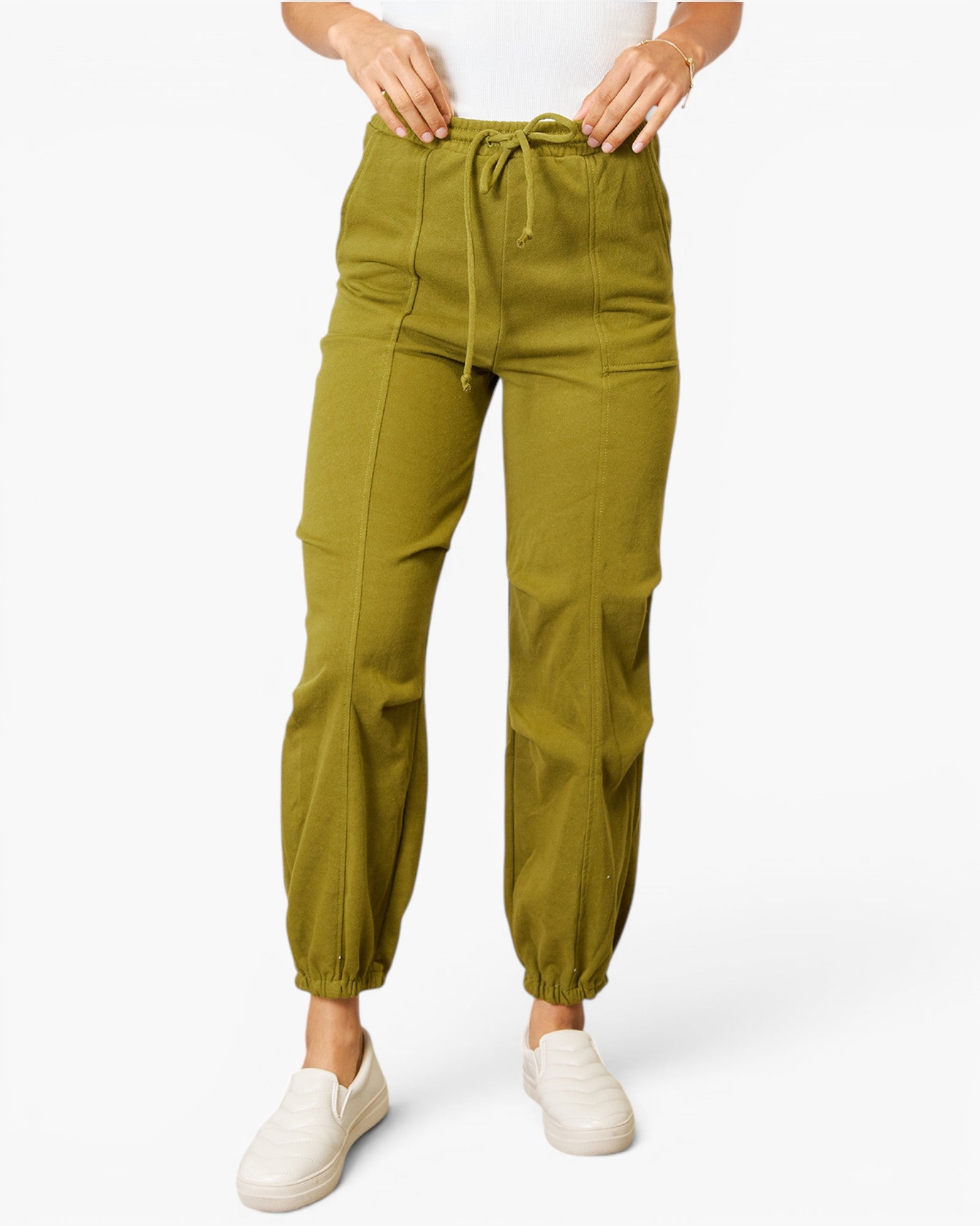 A person wearing olive green drawstring jogger-style pants with elastic cuffs and white slip-on sneakers, shown against a plain light background.