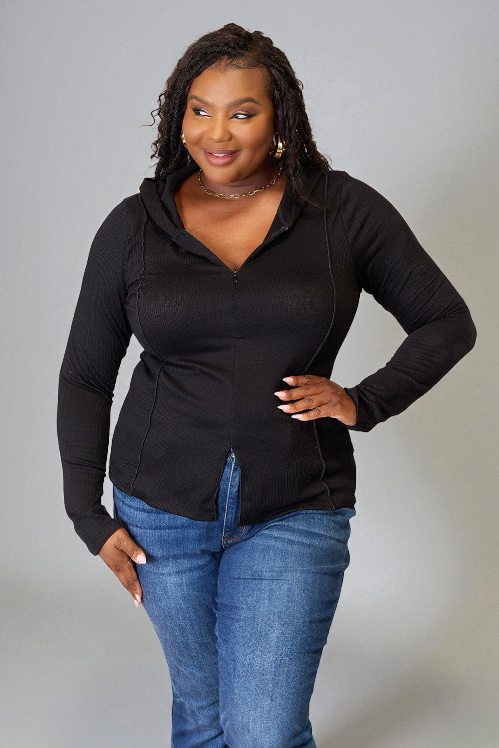 Woman wearing a black zip-up hoodie and blue jeans against a gray background