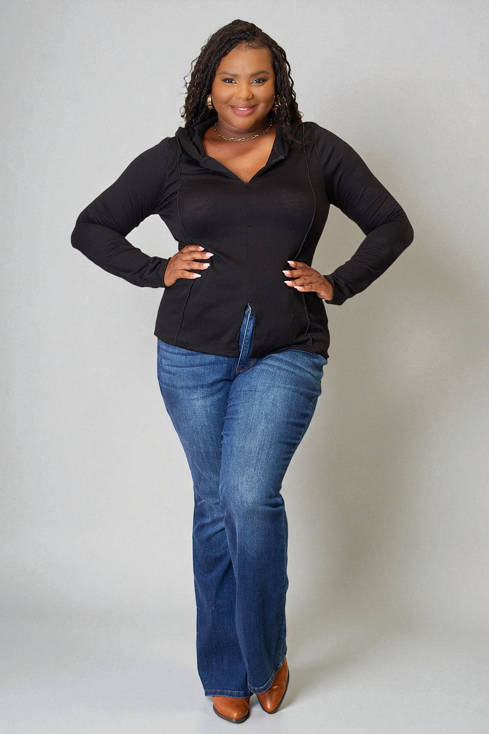 Woman wearing a black long-sleeve top and blue jeans against a plain background