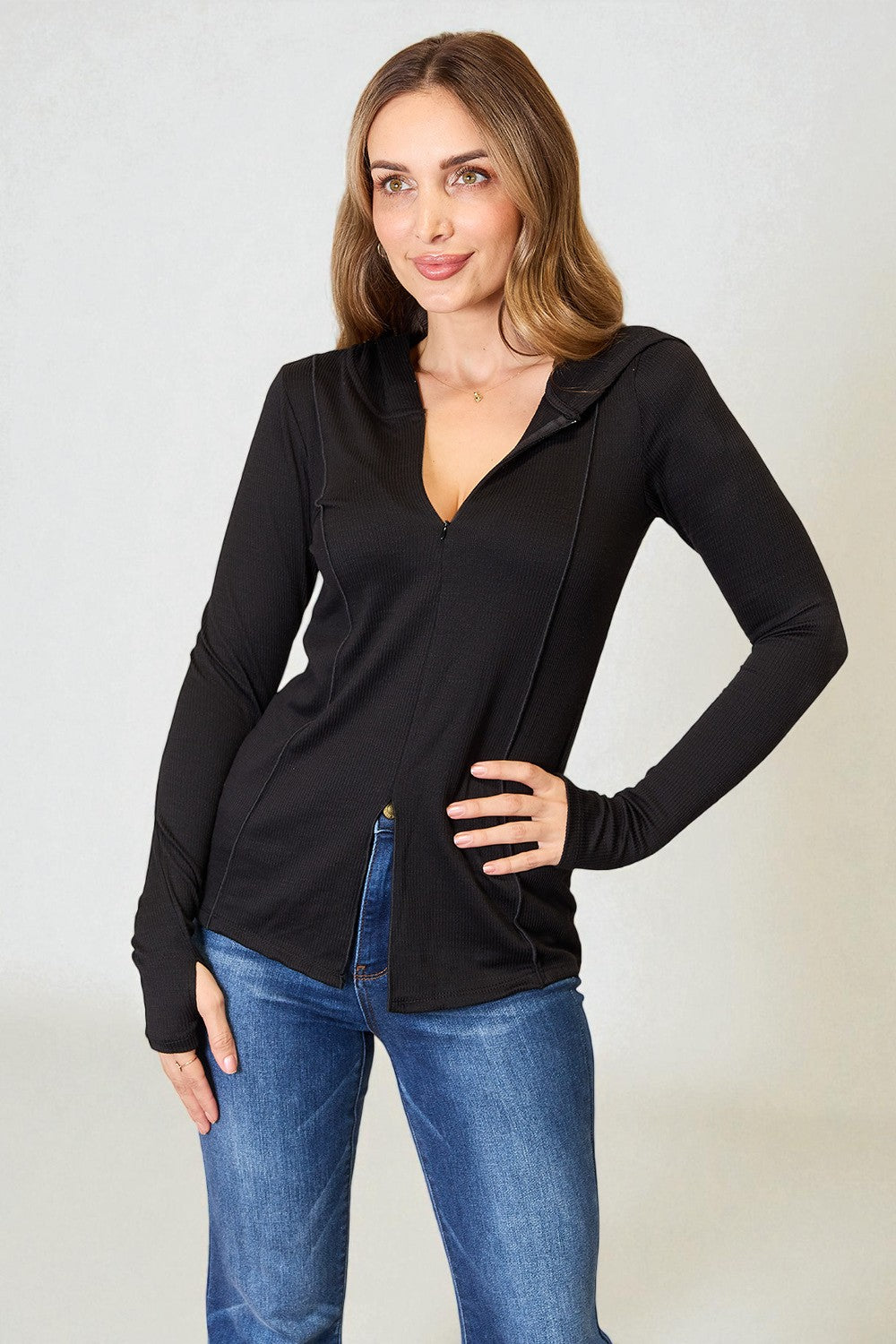 Woman wearing a black long-sleeve top and blue jeans against a plain background