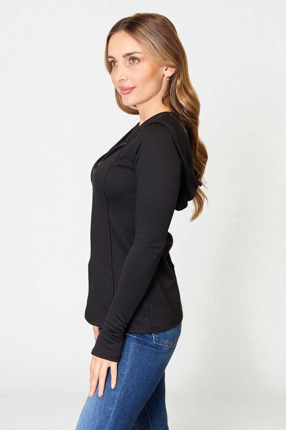 Woman wearing a black long-sleeve top and blue jeans on a white background