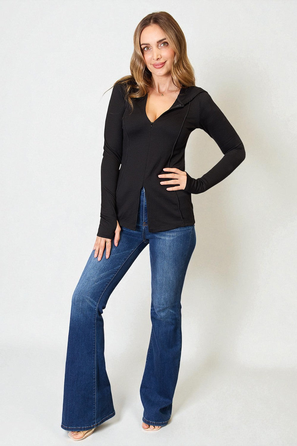 Woman wearing a black long-sleeve top and blue jeans on a white background