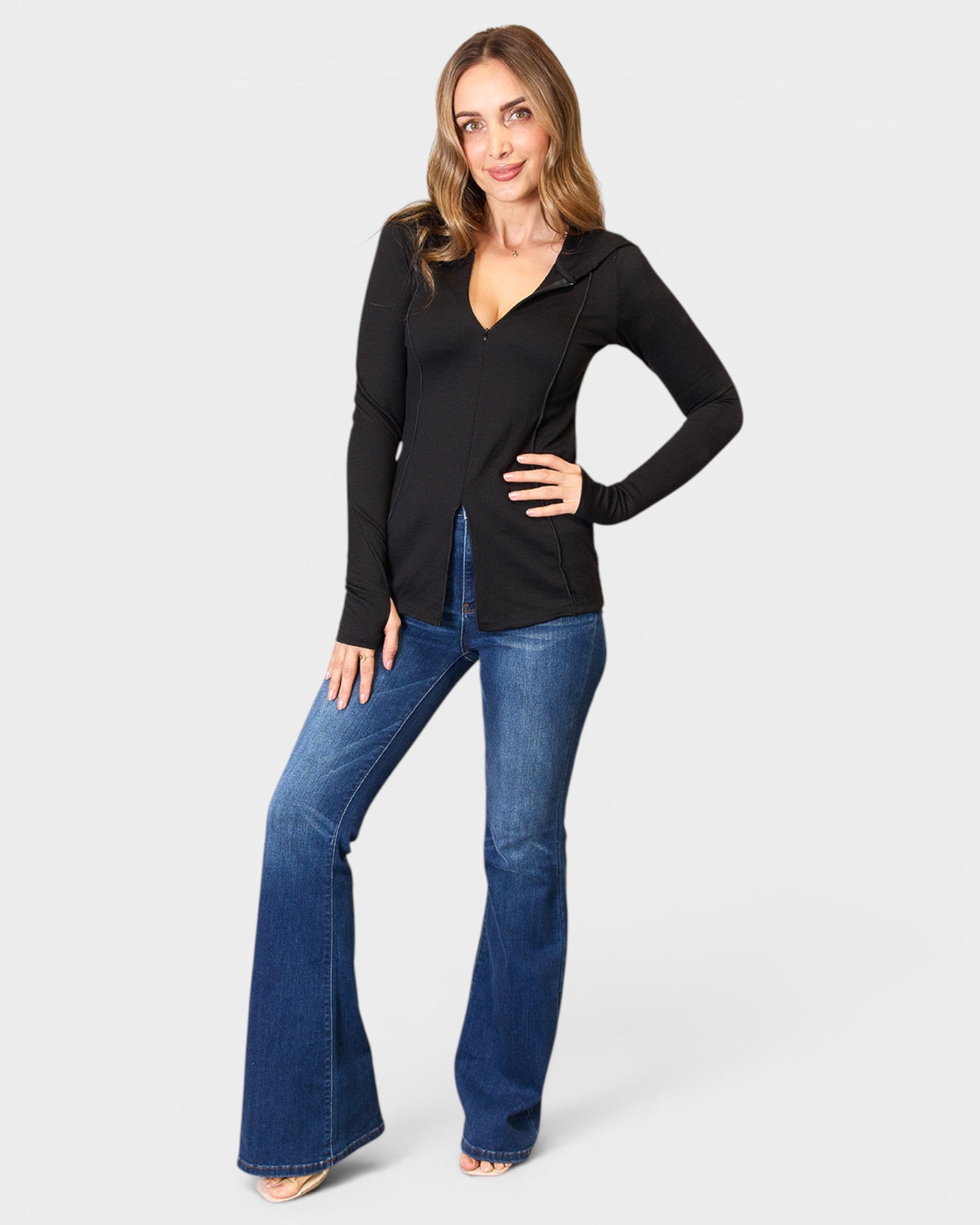 Woman wearing a black long-sleeve top and blue jeans on a white background