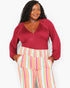 A woman modeling a long-sleeve wrap-style top in deep burgundy paired with pastel pink, yellow, and blue striped pants, against a plain light gray background.
