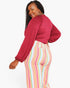 A woman modeling a long-sleeve burgundy top and pastel striped pants against a plain white background.