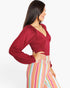 A woman shown in side profile wearing a long-sleeve deep burgundy top and high-waisted striped pants with vertical stripes in pink, yellow, blue, green, and orange, against a plain white background.