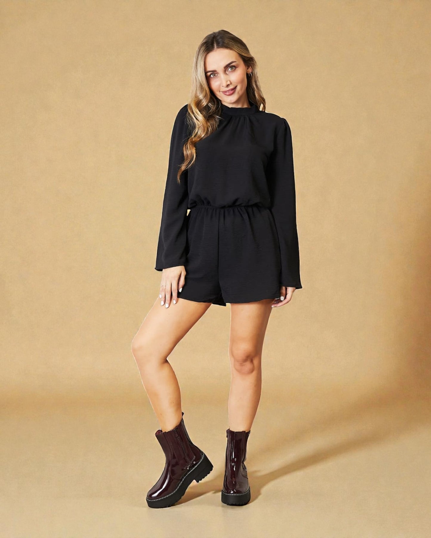 Woman wearing a black outfit with burgundy boots on a beige background