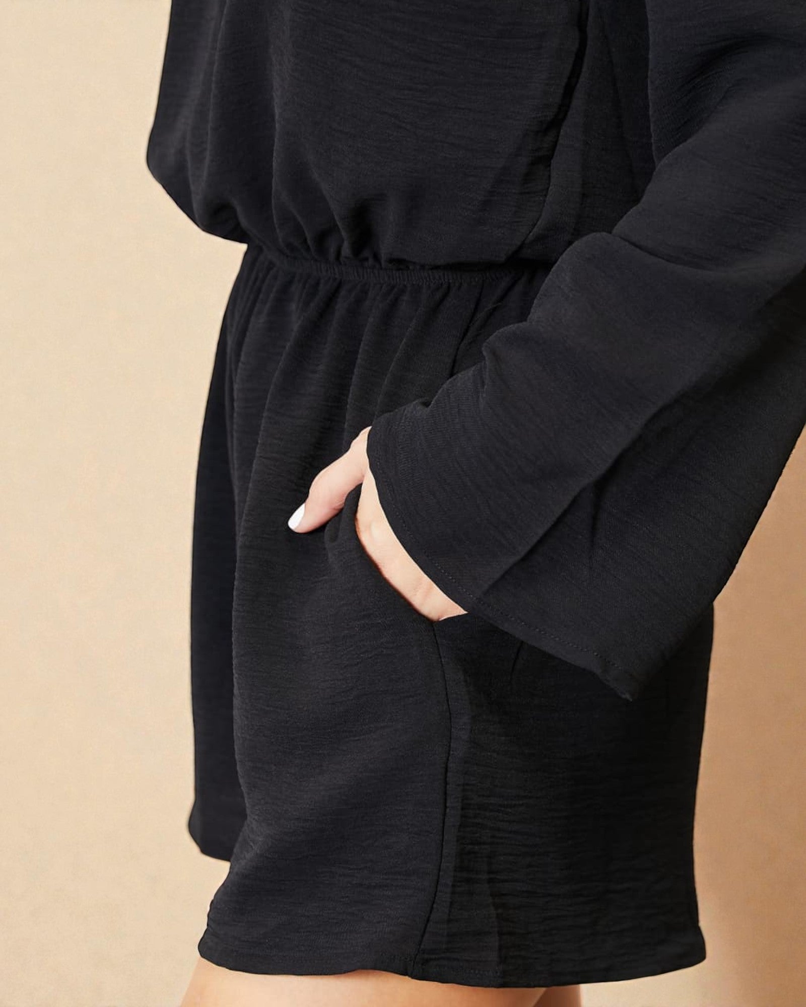 Person wearing a black outfit with long sleeves and shorts on a beige background