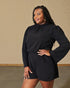Woman wearing a black long-sleeve dress against a beige wall.