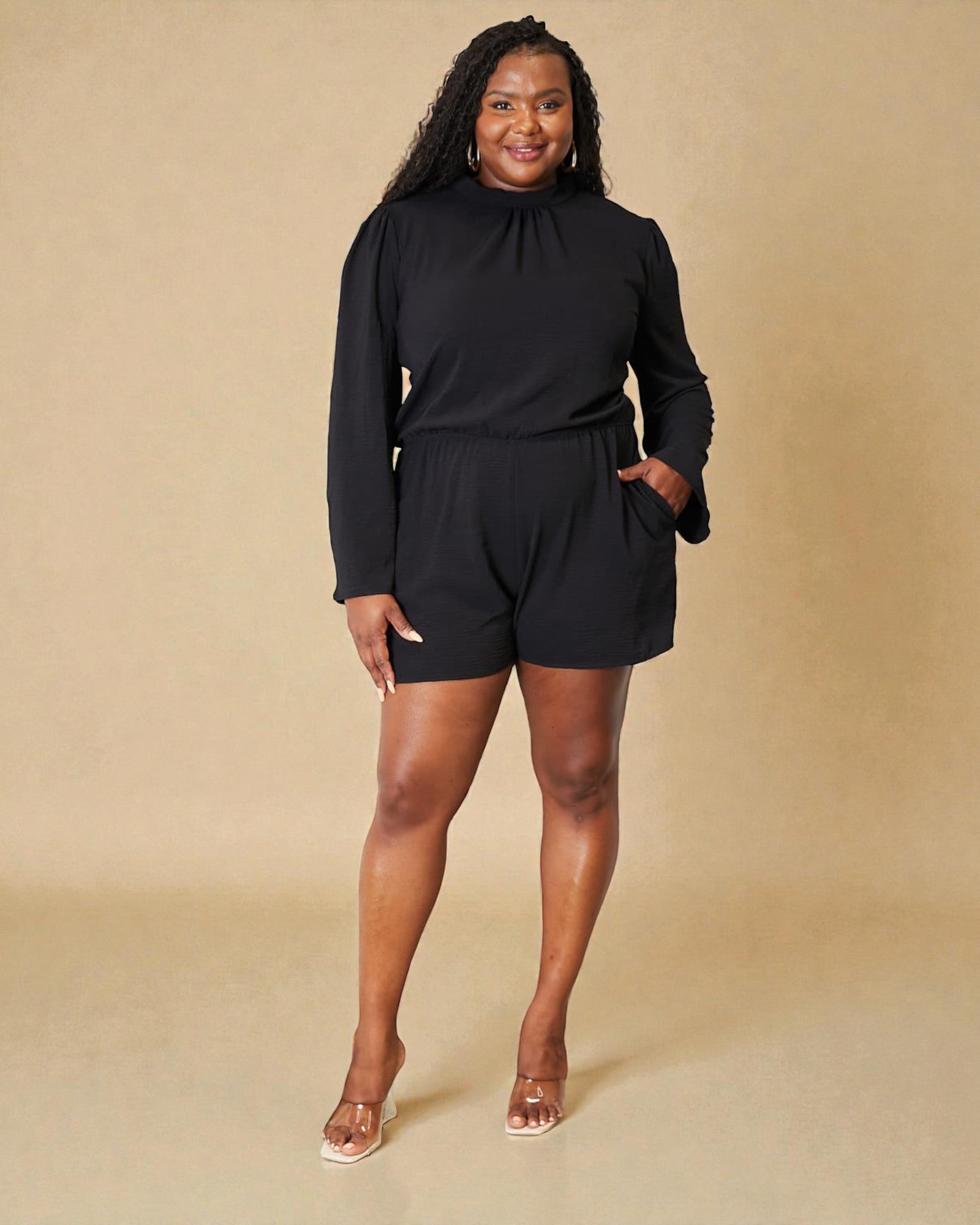 Woman wearing a black long-sleeve romper against a beige background
