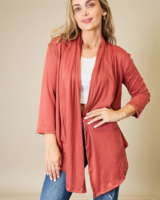 Woman wearing a long, light brown cardigan over a white top and jeans on a beige background