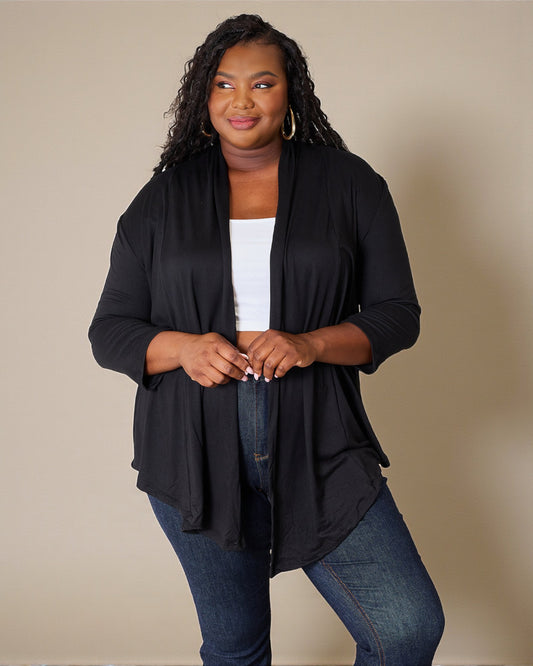 Woman wearing a black cardigan over a white top and blue jeans on a beige background