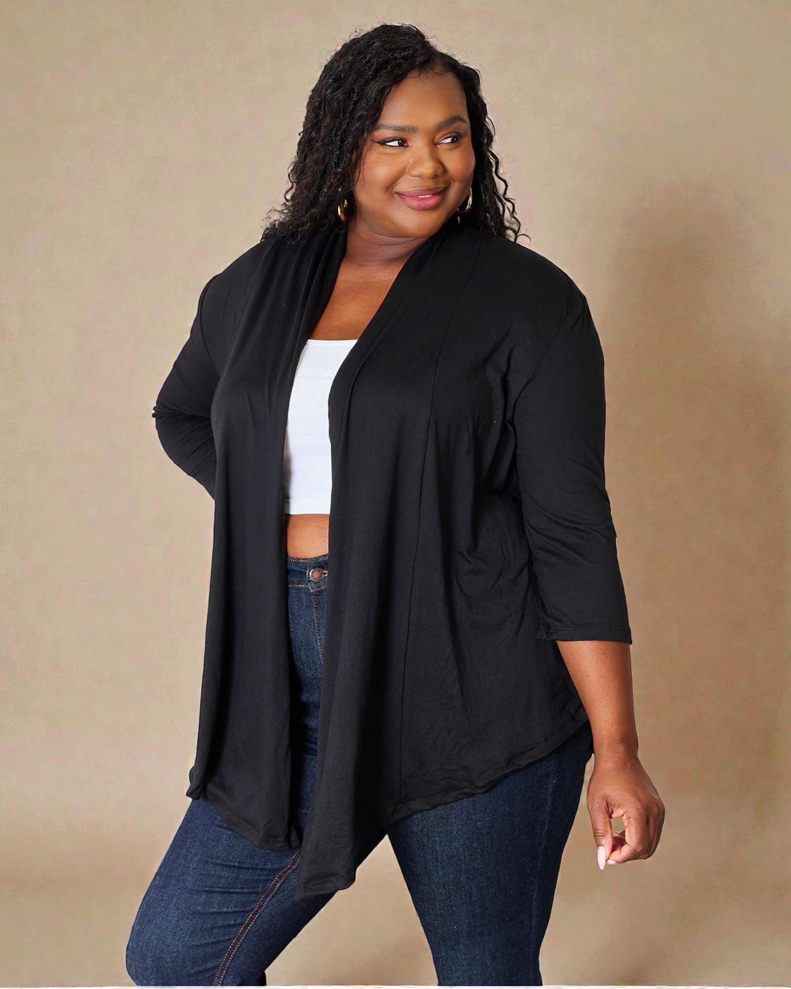 Woman wearing a black cardigan over a white top and blue jeans on a beige background