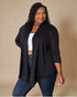 Woman wearing a black cardigan over a white top and blue jeans on a beige background