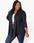 A woman modeling a black open-front cardigan with three-quarter sleeves, worn over a white crop top and blue jeans, against a plain white studio background.