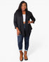 A woman modeling a black open-front cardigan over a white crop top, blue jeans, and brown ankle boots, photographed against a plain light gray studio background.