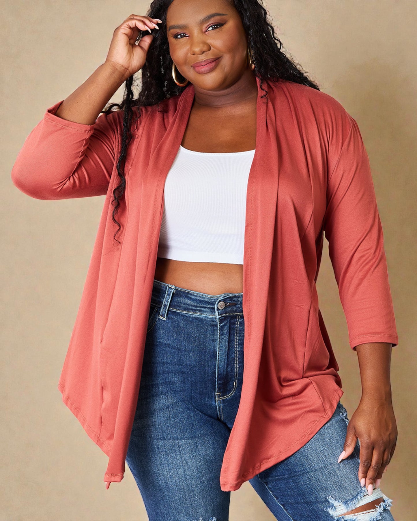 Woman wearing a coral cardigan, white top, and blue jeans on a beige background