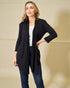 Woman wearing a black cardigan over a white top and jeans on a beige background