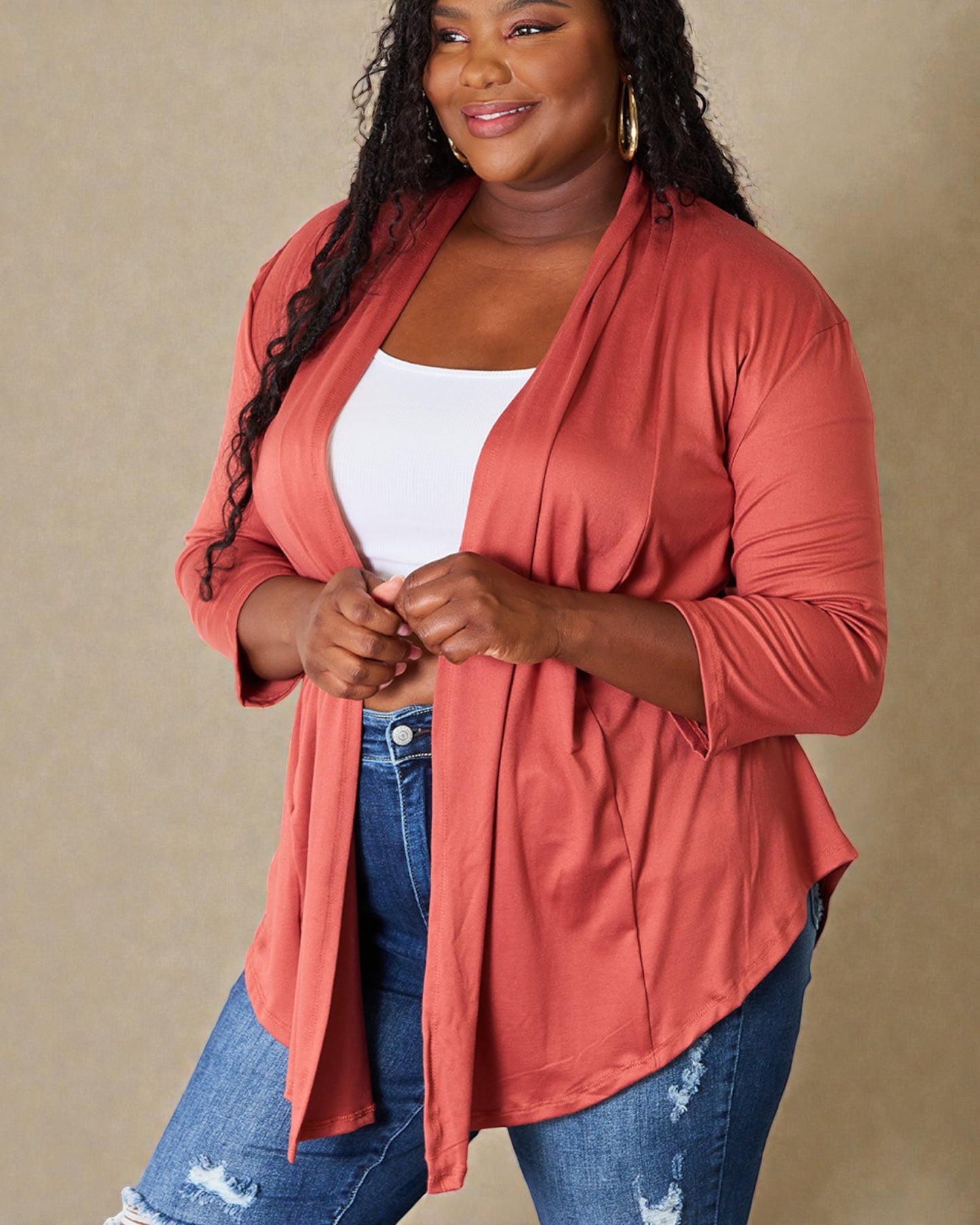 Woman wearing a coral cardigan over a white top and blue jeans on a beige background