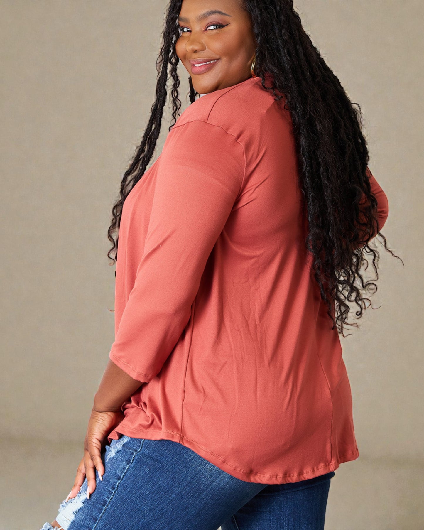 Woman wearing a coral long-sleeve top and blue jeans against a beige background